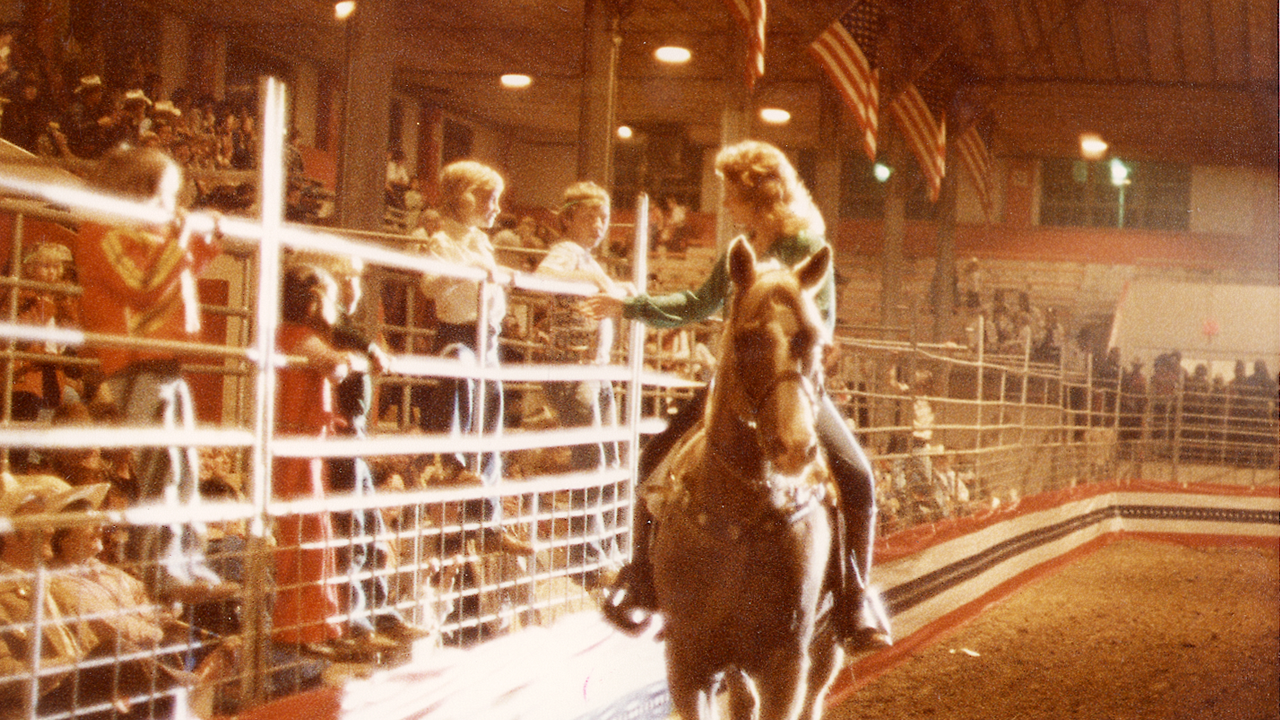 Reba on horseback talking to two young boys on fence 